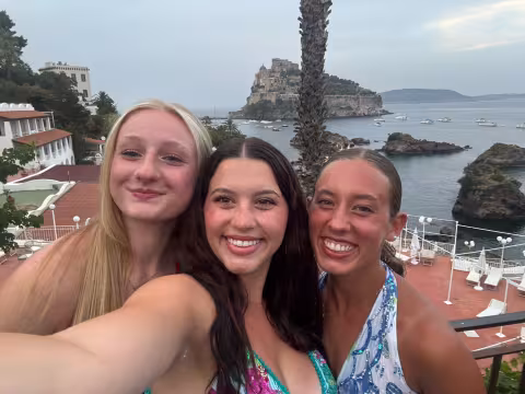 Three girls on a clifftop overlooking blue water taking a selfie.