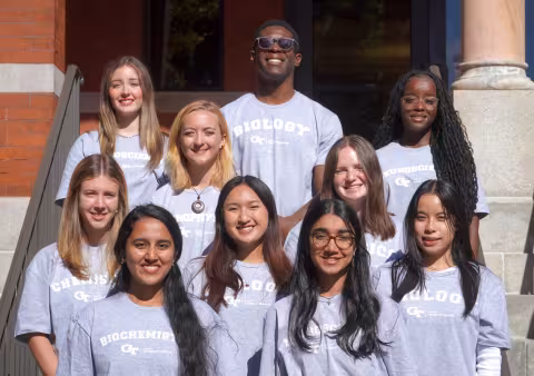 10 students standing in rows in front of brick building.