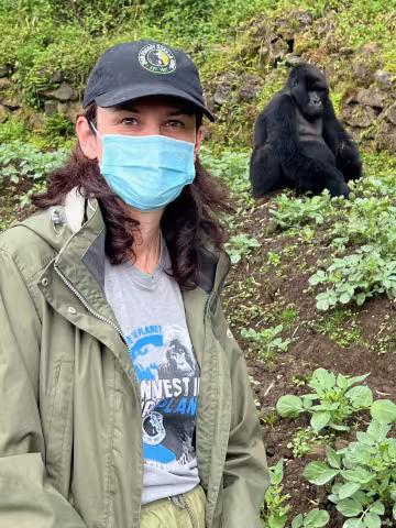 A woman wearing a mask stands near a gorilla.